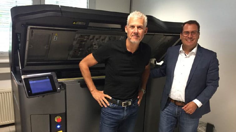 Ein lächelnder Ingenieur in Jeans und Blazer steht vor einer Maschine auf einer Veranstaltung im Bereich des Ingenieurwesens und der Technologie, mit einem Gürtel um die Taille und dem Hintergrund einer Flugreise.
